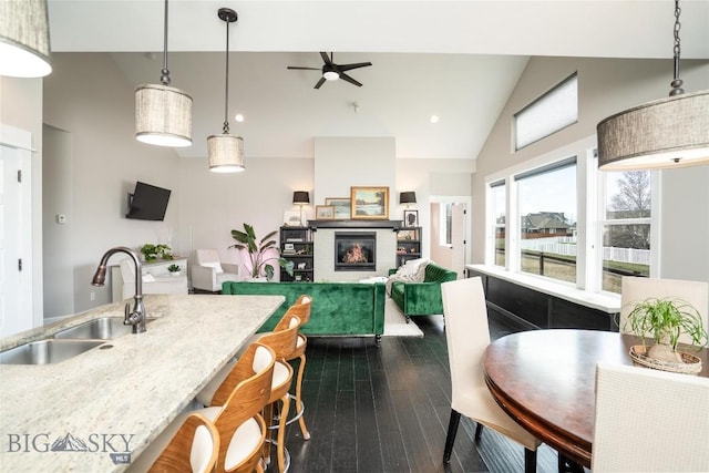 kitchen with a sink, dark wood-style flooring, a glass covered fireplace, ceiling fan, and light stone countertops