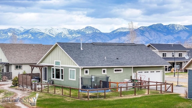 rear view of house with a mountain view, fence, a garage, a shingled roof, and board and batten siding