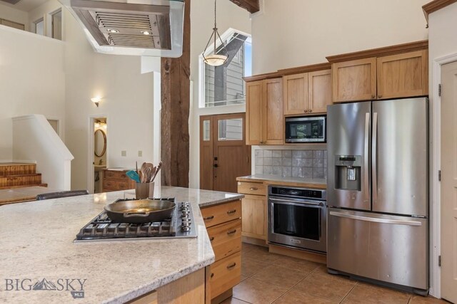 2514 Putter Ct, Bozeman, MT 59715 - kitchen featuring a high ceiling, light tile patterned flooring, light stone countertops, decorative backsplash, and stainless steel appliances