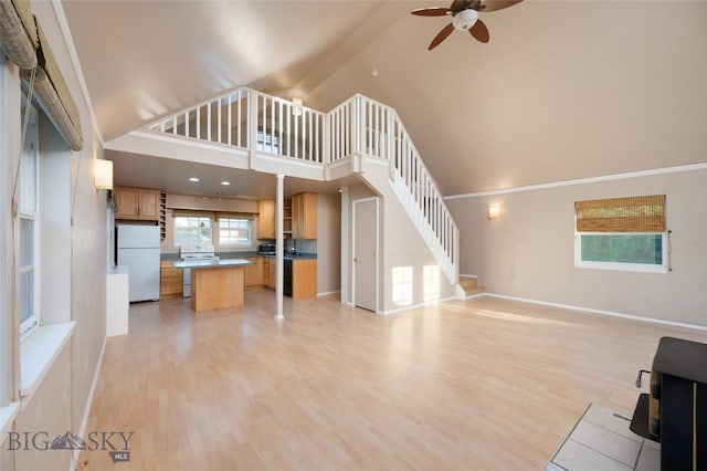 unfurnished living room with light wood finished floors, high vaulted ceiling, stairway, and a ceiling fan