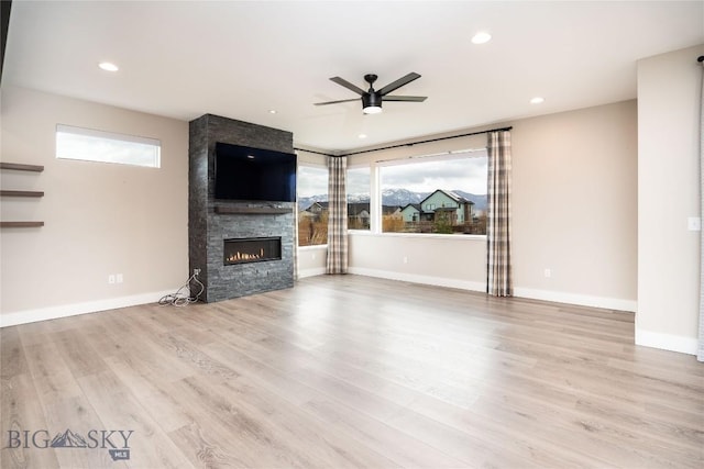 unfurnished living room with wood finished floors, ceiling fan, a large fireplace, and a wealth of natural light
