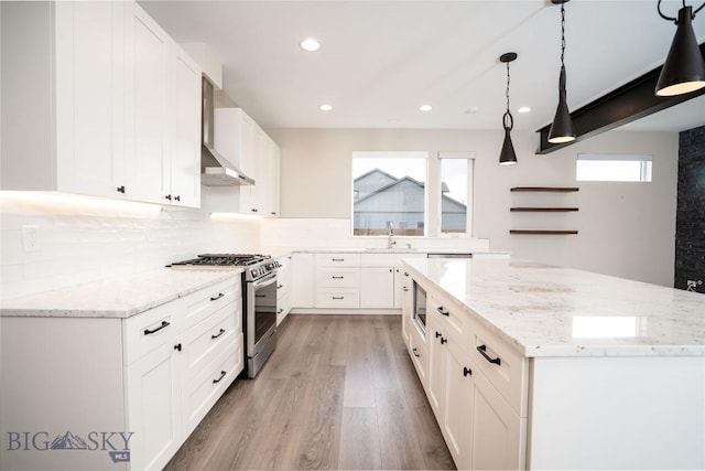 kitchen with white cabinets, wall chimney exhaust hood, stainless steel range with gas cooktop, backsplash, and a kitchen island