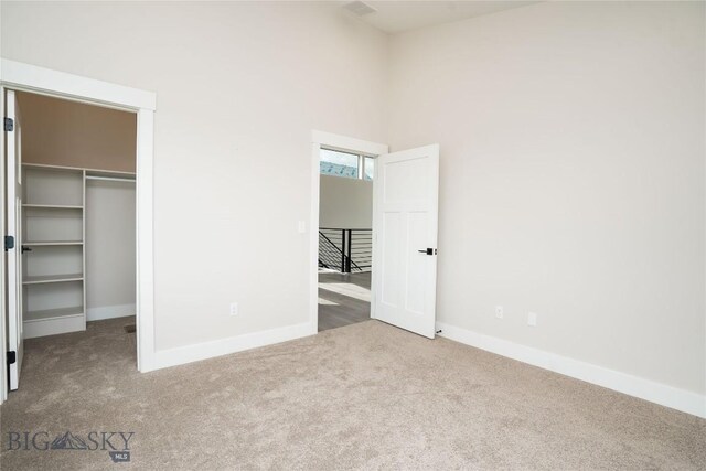 unfurnished bedroom featuring a high ceiling, carpet flooring, baseboards, and a walk in closet