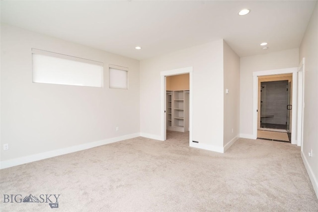 unfurnished bedroom featuring light carpet, baseboards, a spacious closet, and recessed lighting