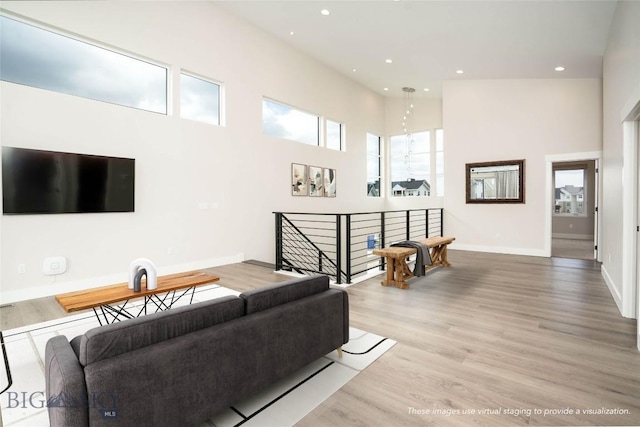 living room featuring light wood-style flooring, recessed lighting, a high ceiling, and baseboards