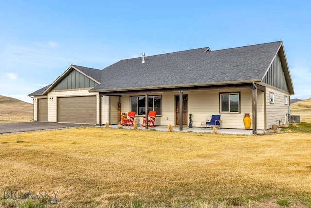 single story home with aphalt driveway, board and batten siding, an attached garage, a front yard, and roof with shingles