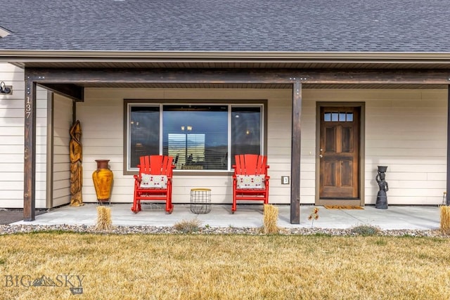 entrance to property with roof with shingles, a porch, and a yard