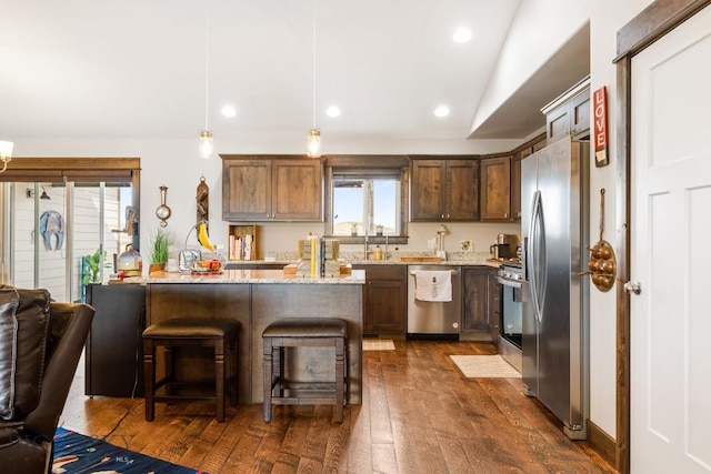 kitchen featuring dark wood finished floors, a breakfast bar, vaulted ceiling, light stone countertops, and appliances with stainless steel finishes