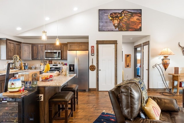 kitchen featuring high vaulted ceiling, light stone counters, a breakfast bar, pendant lighting, and appliances with stainless steel finishes