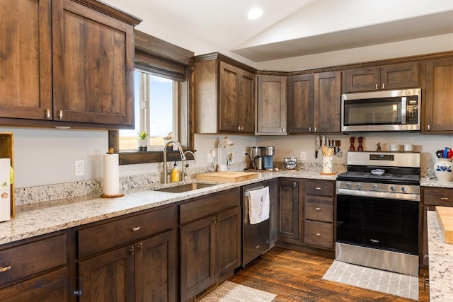 kitchen featuring dark brown cabinets, vaulted ceiling, a sink, appliances with stainless steel finishes, and dark wood-style flooring