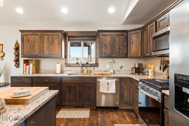 kitchen featuring dark brown cabinets, a sink, appliances with stainless steel finishes, light stone countertops, and dark wood-style floors