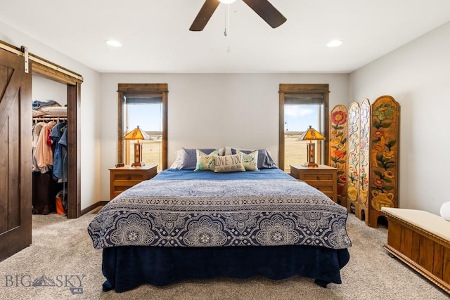 bedroom with a barn door, a closet, a walk in closet, light carpet, and recessed lighting
