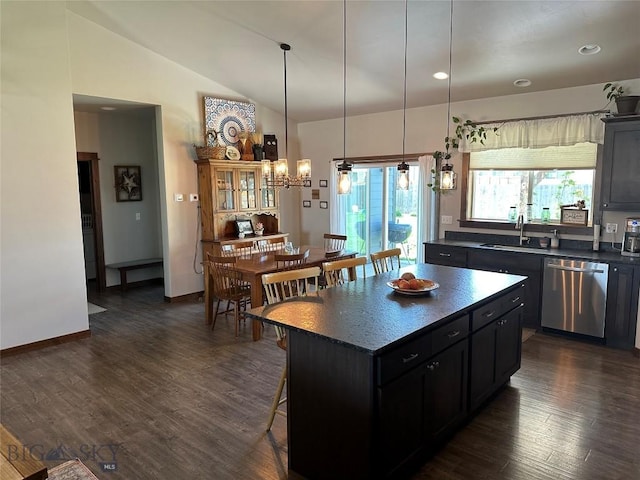 kitchen with stainless steel dishwasher, dark countertops, a kitchen bar, dark cabinets, and a sink