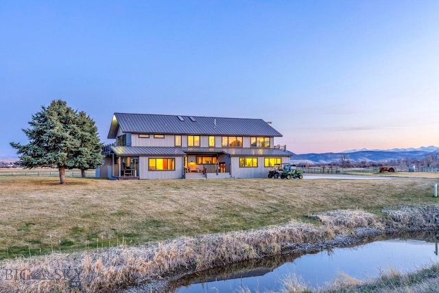 back of house at dusk featuring a lawn, a mountain view, and metal roof