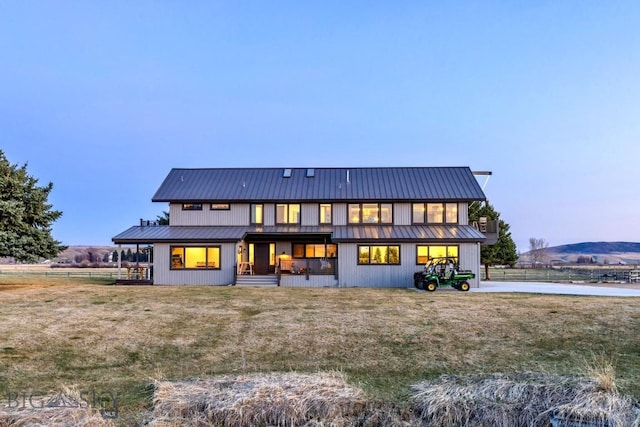 back of house at dusk featuring a lawn and metal roof