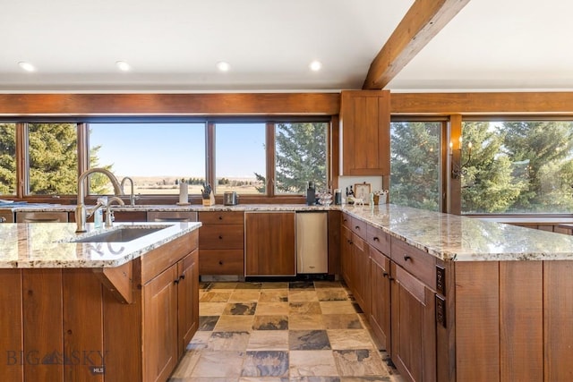 kitchen with a sink, plenty of natural light, stone finish flooring, a peninsula, and light stone countertops