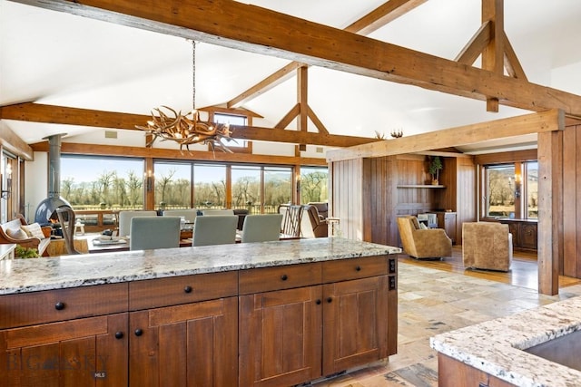 kitchen featuring light stone counters, open floor plan, a chandelier, and beamed ceiling