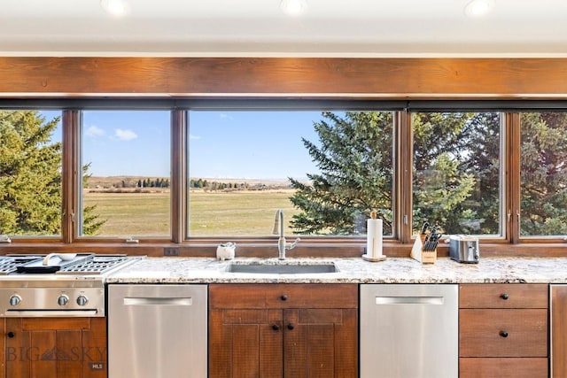 kitchen with brown cabinets, dishwasher, light stone countertops, and a sink