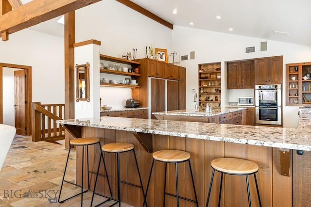 kitchen with stainless steel appliances, a sink, a kitchen bar, open shelves, and high vaulted ceiling