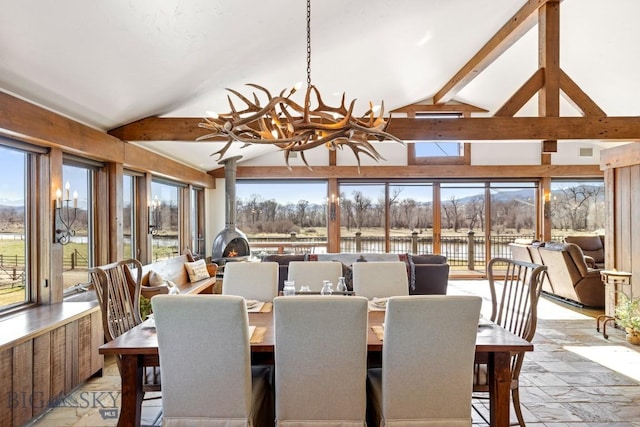 dining room with a wood stove, a notable chandelier, lofted ceiling with beams, and a water view