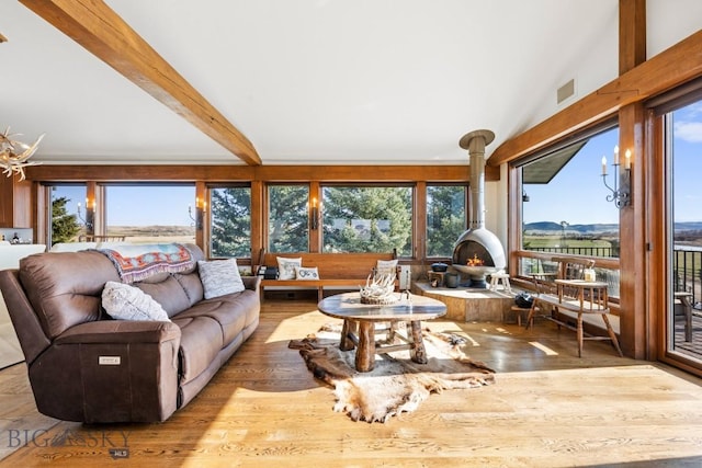 living room featuring beamed ceiling, a wood stove, wood finished floors, and visible vents