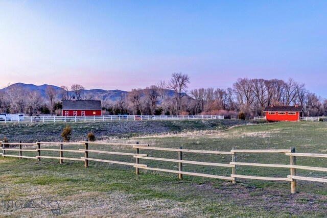 yard at dusk featuring fence, a rural view, an outbuilding, and a mountain view