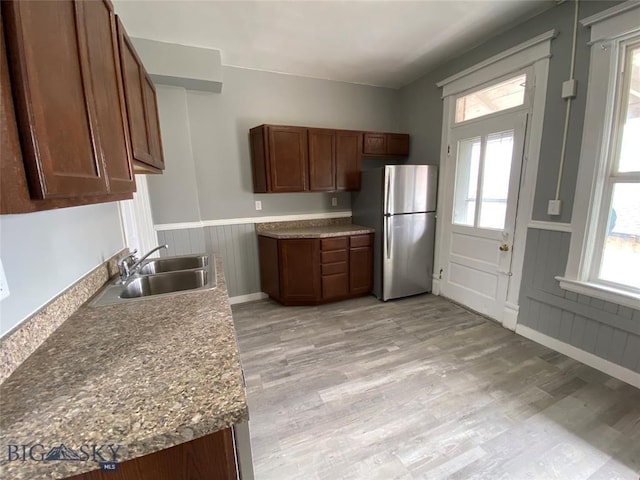 kitchen featuring freestanding refrigerator, light wood finished floors, wainscoting, and a sink