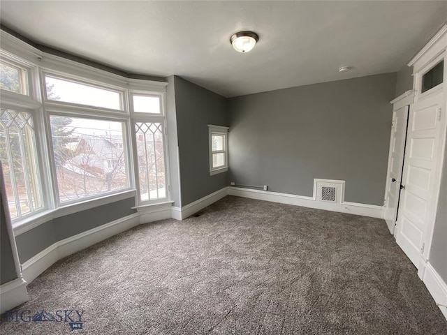 empty room featuring baseboards, dark colored carpet, and visible vents