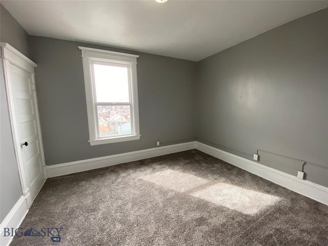 empty room featuring baseboards and dark colored carpet