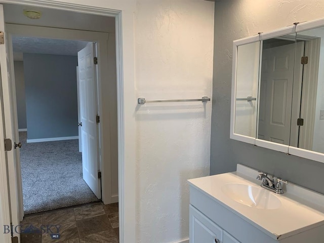 bathroom featuring baseboards, a textured wall, and vanity