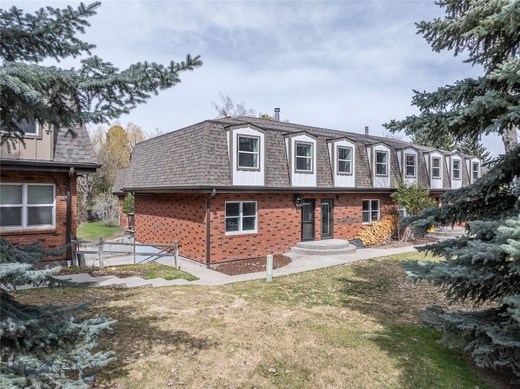 back of house featuring a lawn, brick siding, a shingled roof, and mansard roof