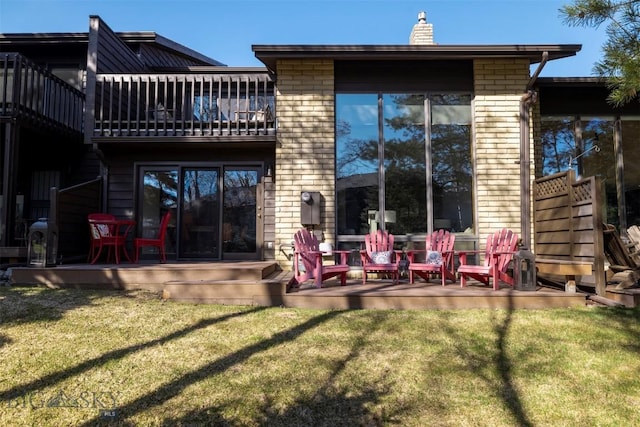 rear view of property featuring brick siding, a lawn, a chimney, and a balcony