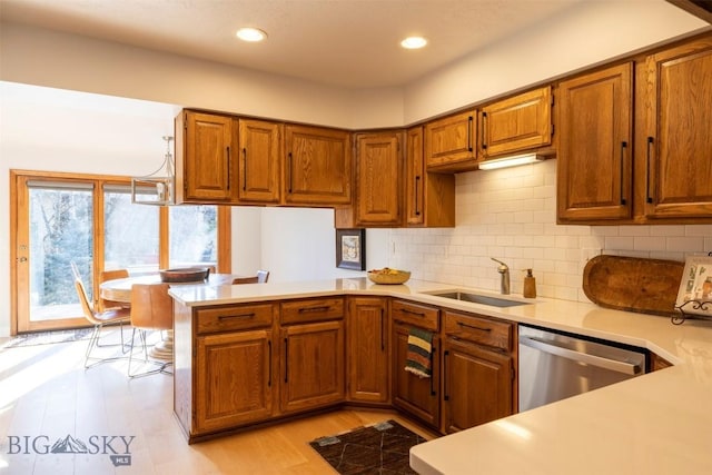 kitchen featuring light countertops, stainless steel dishwasher, a sink, a peninsula, and brown cabinetry