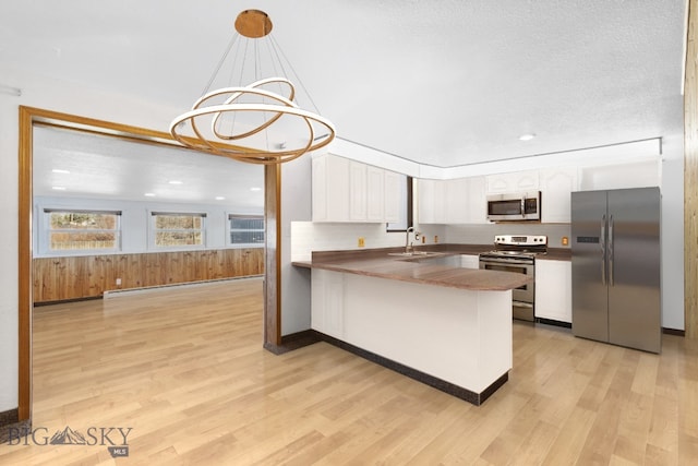 509 1st E, Whitehall, MT 59759 - kitchen with stainless steel appliances, a peninsula, white cabinetry, light wood-style flooring, and dark countertops