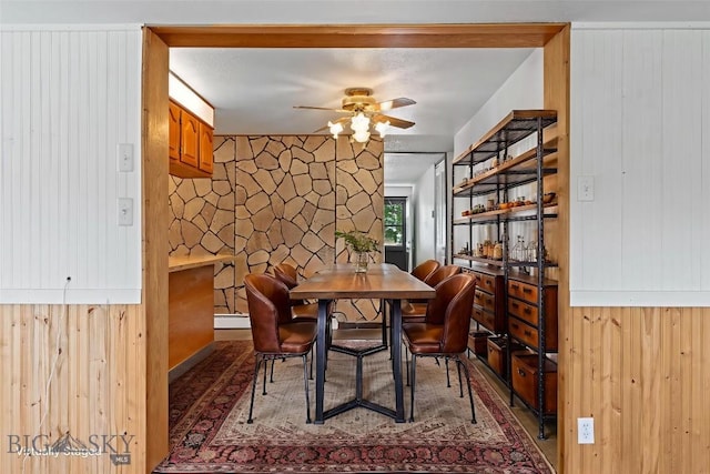 509 1st E, Whitehall, MT 59759 - dining room featuring ceiling fan, a baseboard heating unit, wood finished floors, and wood walls