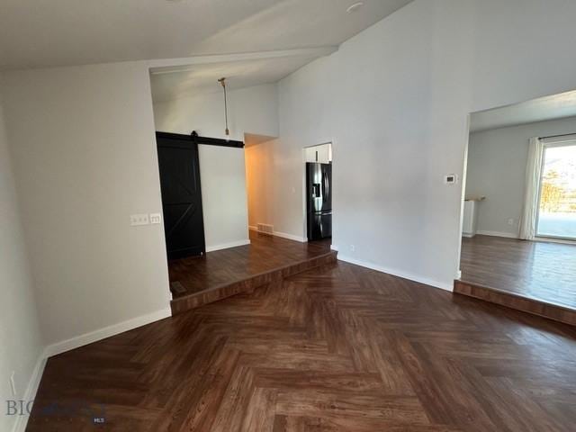spare room with a barn door, baseboards, and high vaulted ceiling