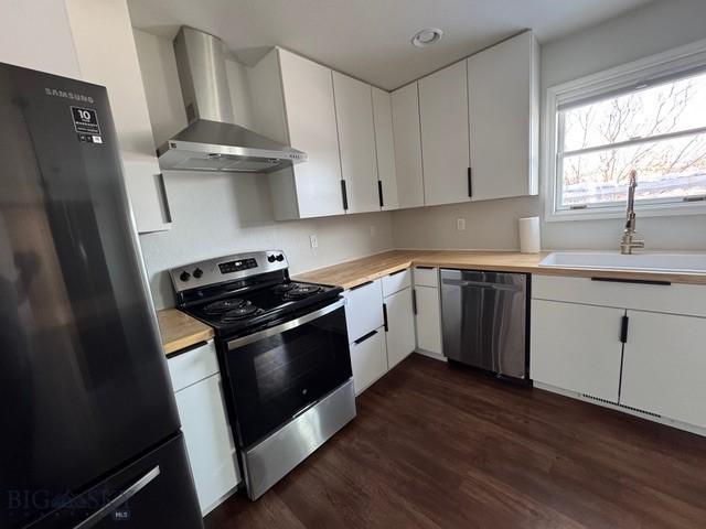 kitchen with light countertops, wall chimney exhaust hood, appliances with stainless steel finishes, and a sink