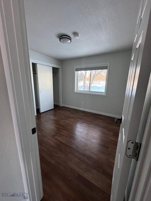 unfurnished bedroom with dark wood finished floors, baseboards, and a closet