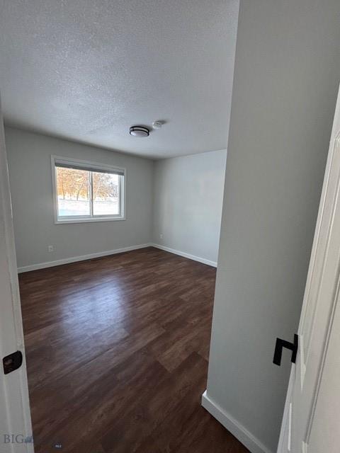 empty room with baseboards, a textured ceiling, and dark wood-style floors