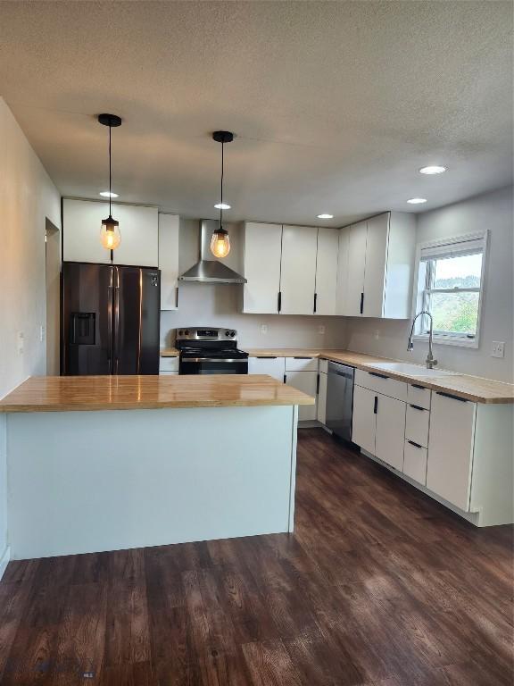 1421 Bluebird Ln, Bozeman, MT 59715 - kitchen with appliances with stainless steel finishes, wall chimney range hood, butcher block counters, dark wood finished floors, and decorative light fixtures