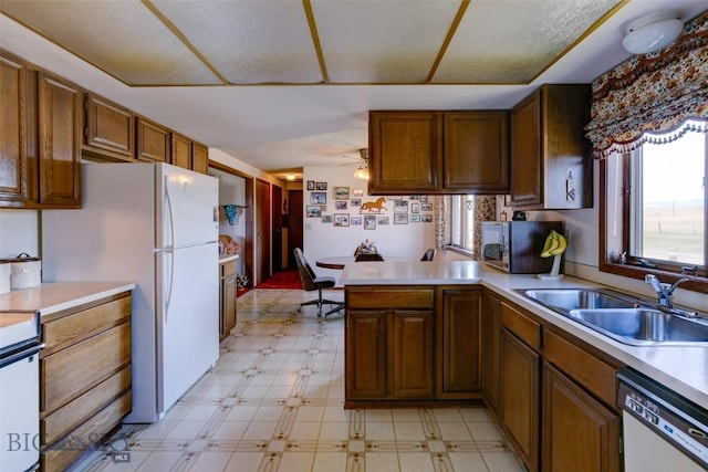 kitchen featuring light floors, a peninsula, white appliances, and a sink