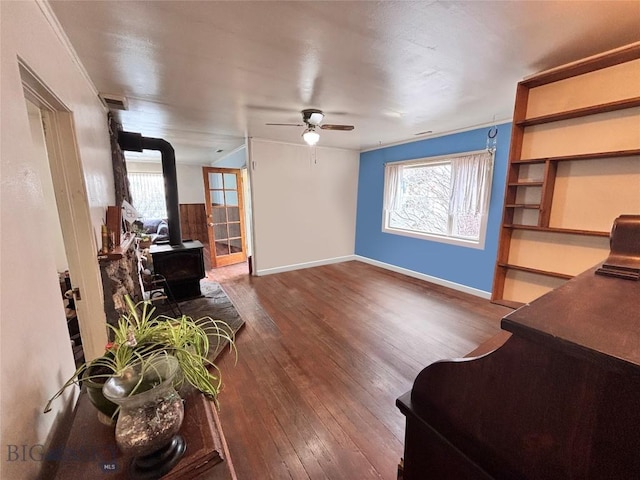 living area with hardwood / wood-style floors, a ceiling fan, baseboards, and a wood stove
