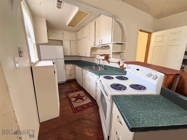 kitchen featuring dark countertops, open shelves, a sink, white appliances, and dark wood-style floors
