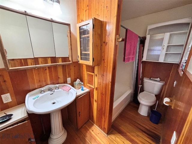 full bathroom with wood walls, shower / bathtub combination with curtain, toilet, a sink, and hardwood / wood-style flooring