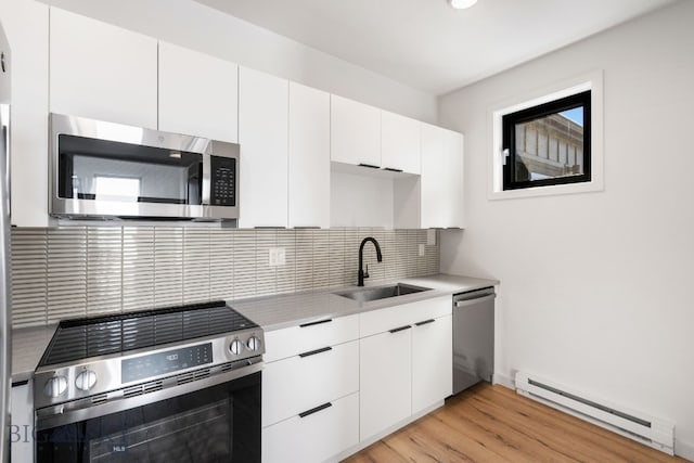 kitchen featuring white cabinets, stainless steel appliances, backsplash, a sink, and a baseboard heating unit