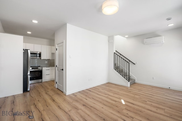 kitchen with white cabinets, light wood-style flooring, a wall unit AC, recessed lighting, and appliances with stainless steel finishes