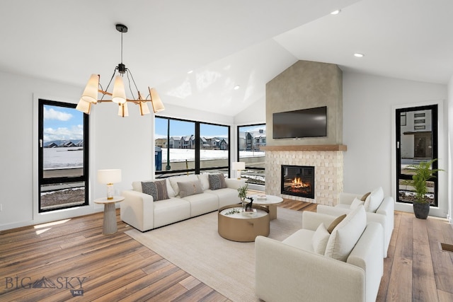 living area featuring vaulted ceiling, wood finished floors, a fireplace, a notable chandelier, and recessed lighting