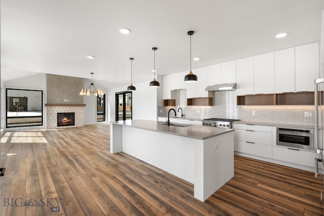 kitchen featuring modern cabinets, under cabinet range hood, a sink, and dark wood-style flooring