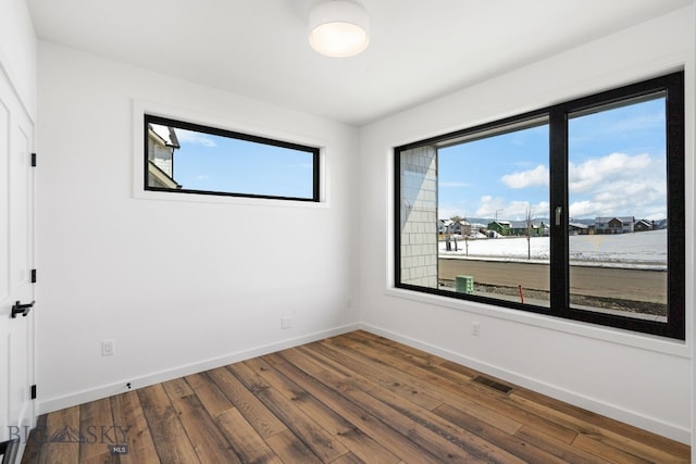 empty room featuring hardwood / wood-style floors, baseboards, and visible vents