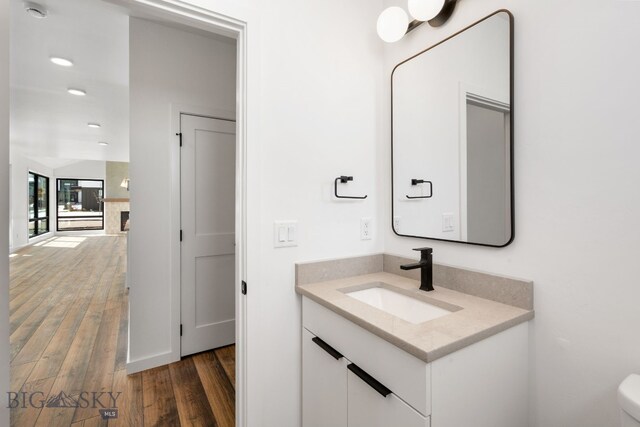 half bathroom with toilet, vanity, wood finished floors, and recessed lighting
